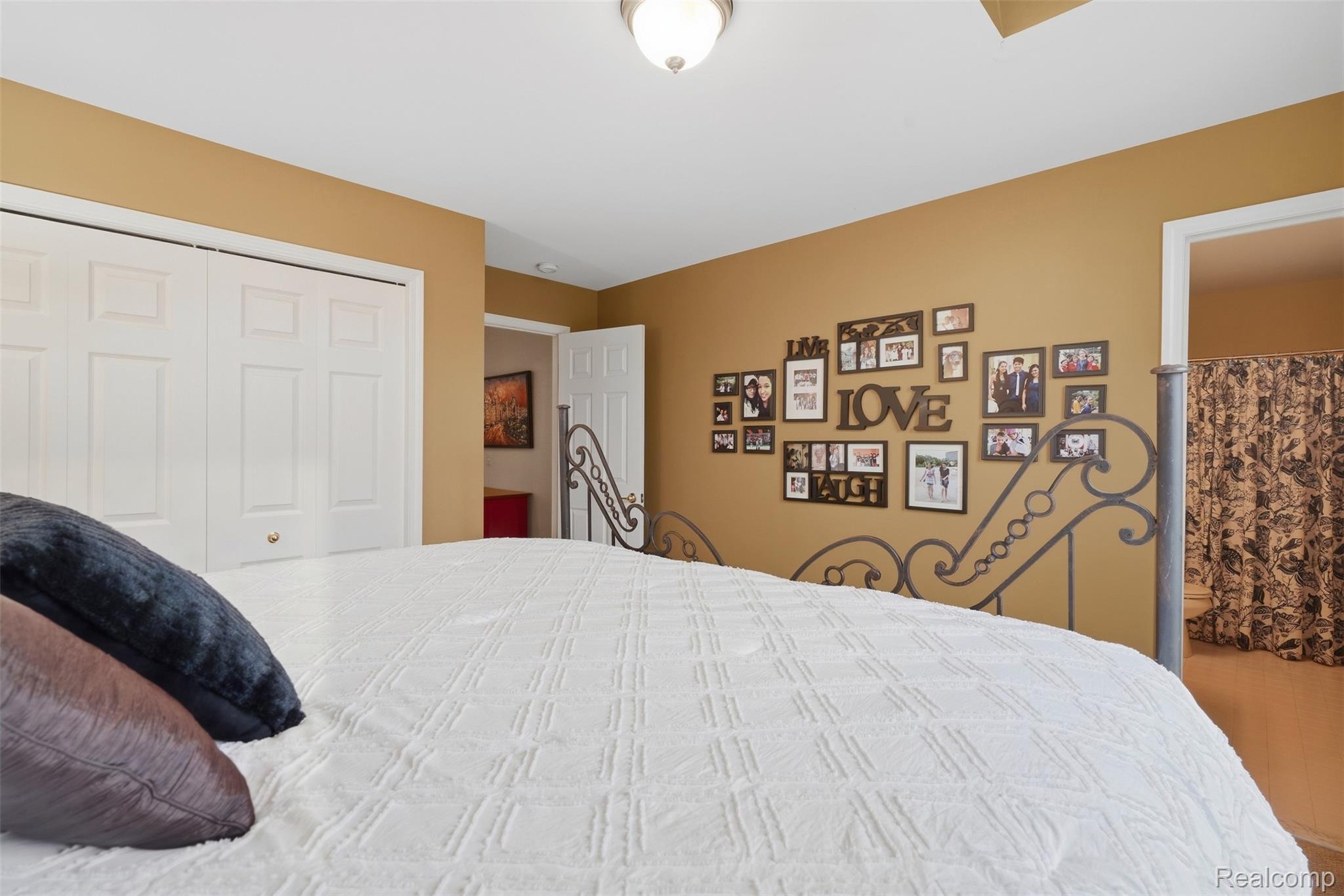 Bedroom with a white quilted bed, ornate metal headboard, and family photo gallery.