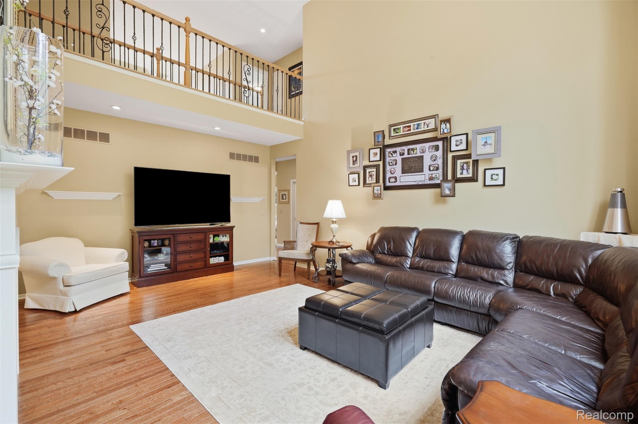 Two-story living room with a dark leather sectional, hardwood floors, and an open gallery above.