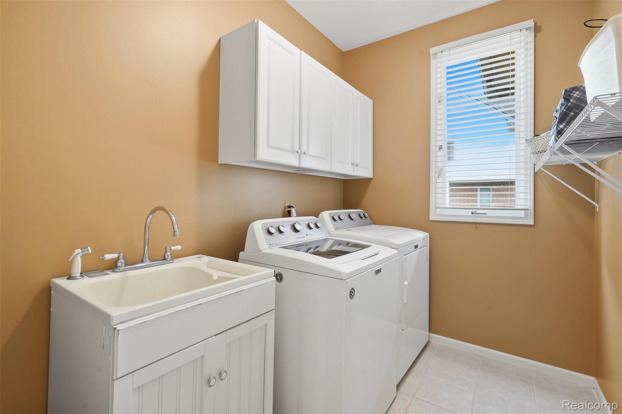 Laundry room with washer and dryer, utility sink, and white wall cabinets.