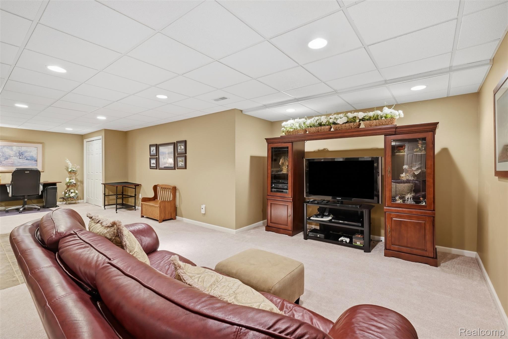Finished basement entertainment room with a large TV cabinet, leather sectional, and desk area.