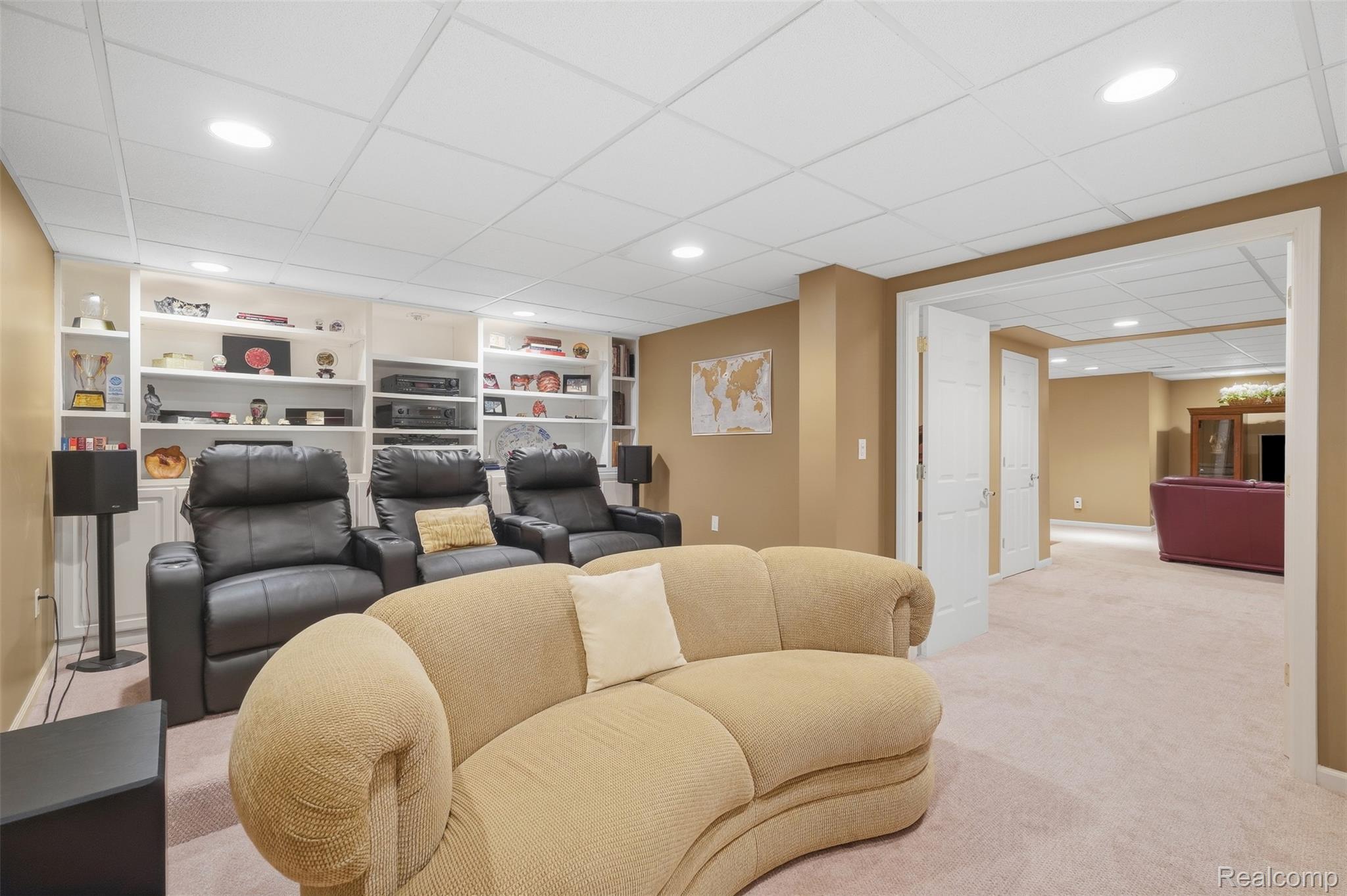 Basement media room with a beige sofa, black recliners, and built-in shelving.