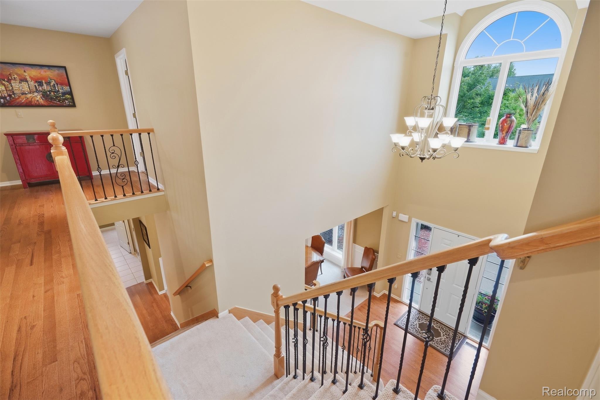 Two-story foyer with carpeted staircase, wood railings, arched window, chandelier, and front entry.