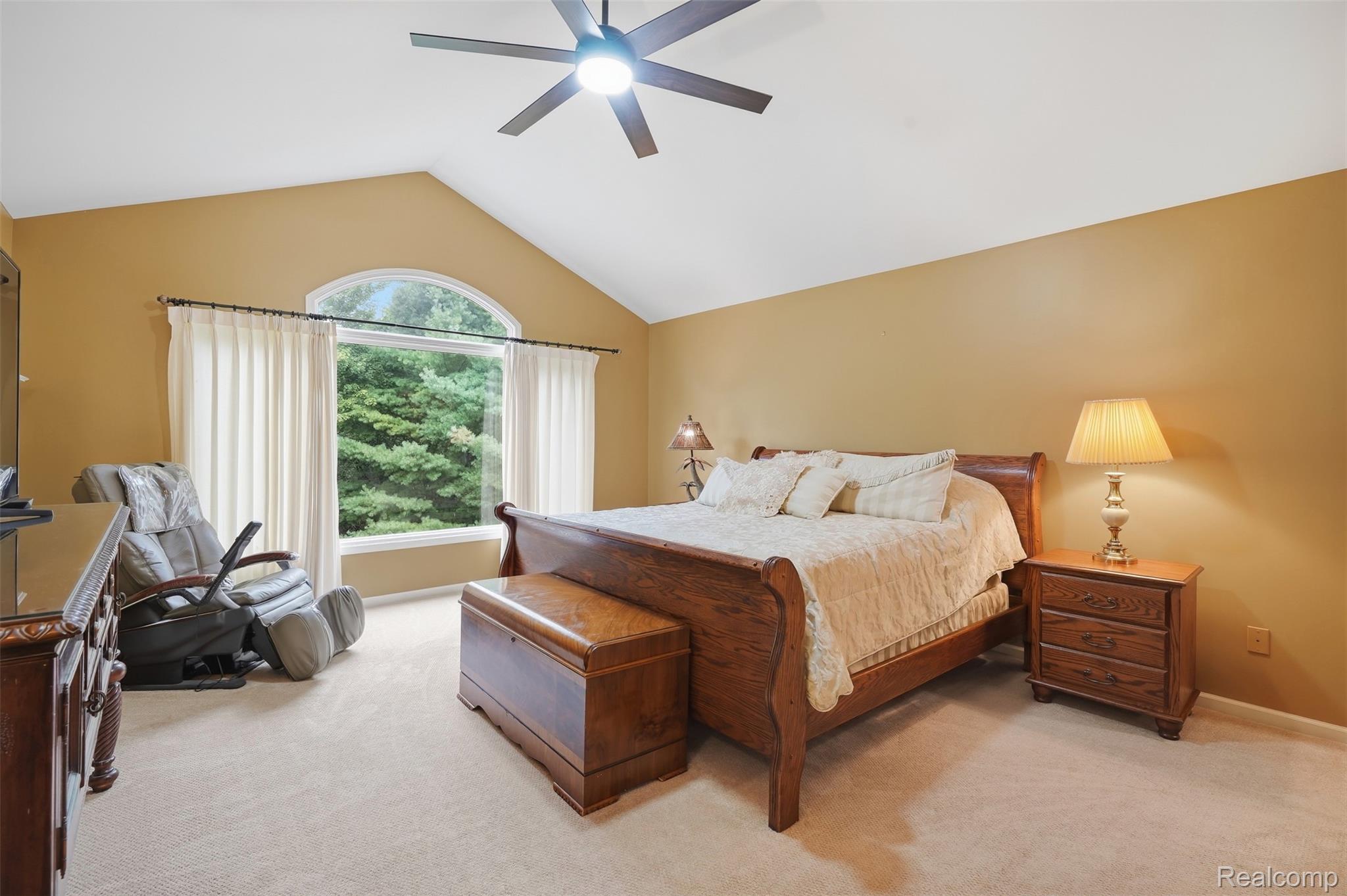 Furnished bedroom with a dark wood sleigh bed, vaulted ceiling, and arched window overlooking trees.