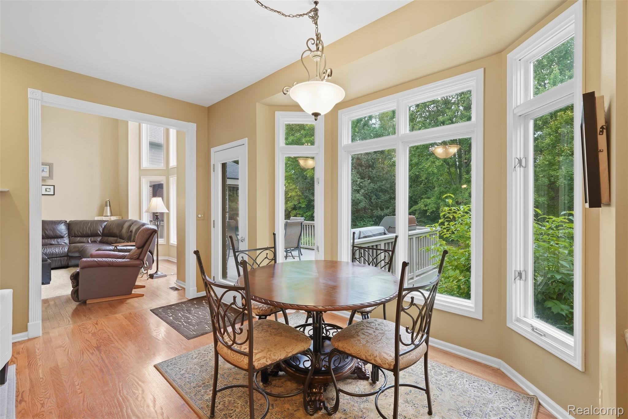 Dining room with a round wooden table, large windows, and a view of a leafy deck.
