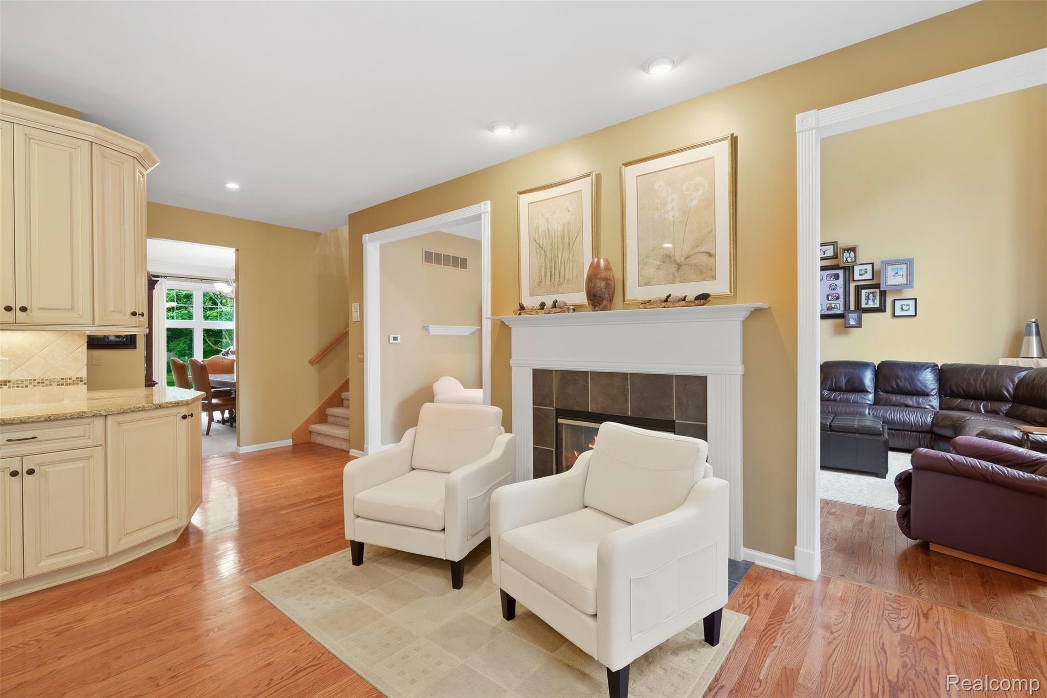 Living room with white armchairs, a fireplace, hardwood floors, and an adjoining family room.