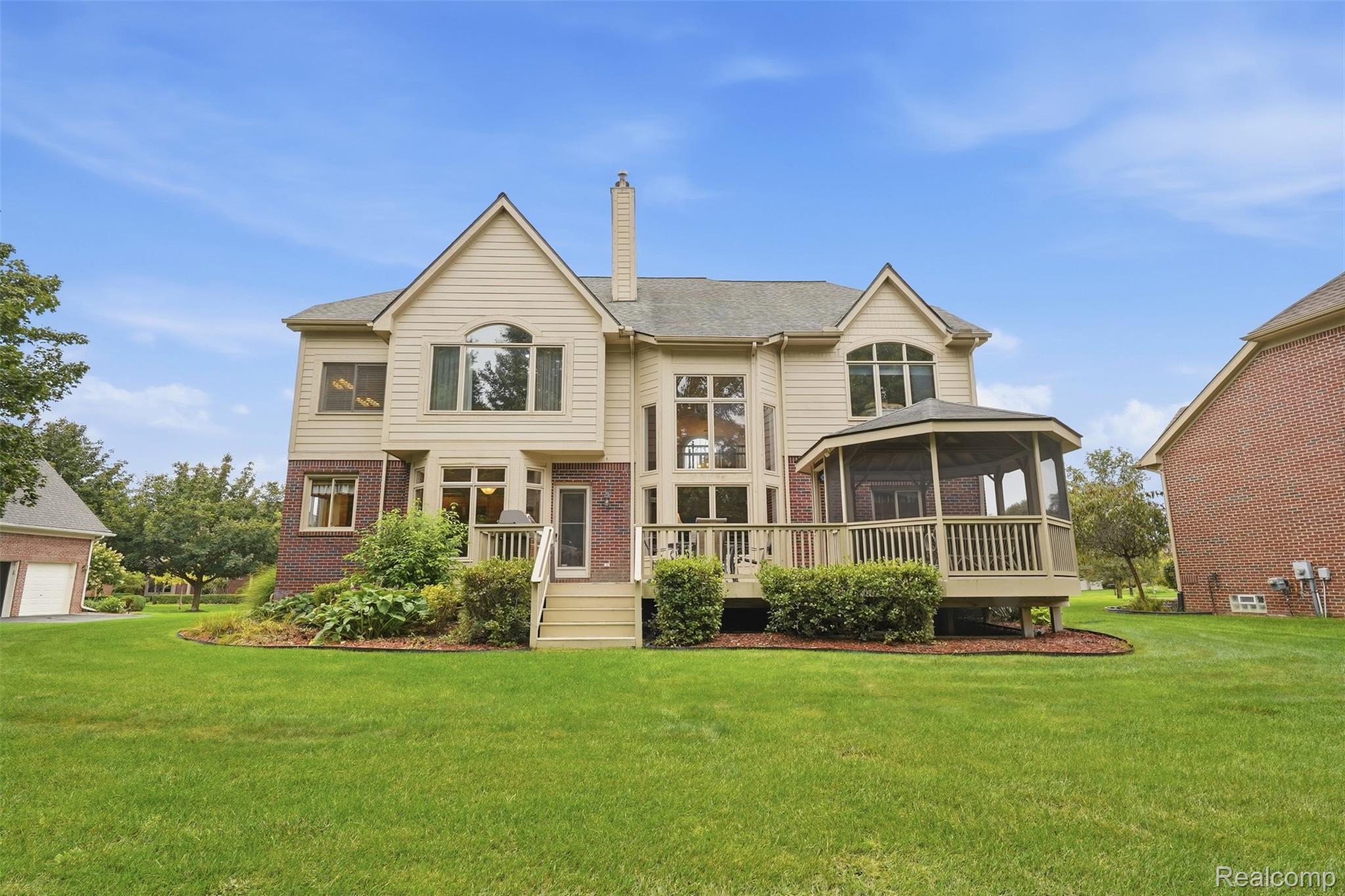 Rear of a two-story home with a covered deck, landscaped garden beds, and a broad lawn.