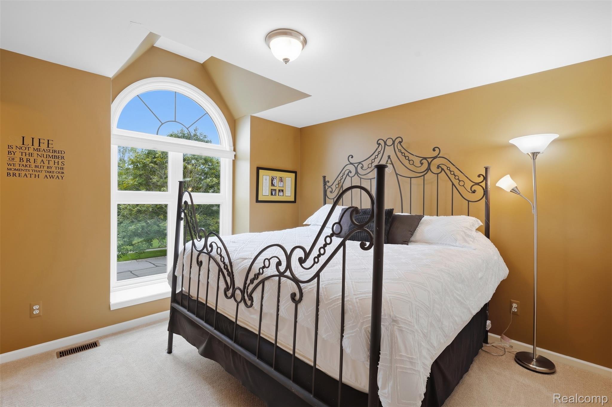 Bedroom with an ornate black metal bed frame beside a large arched window.