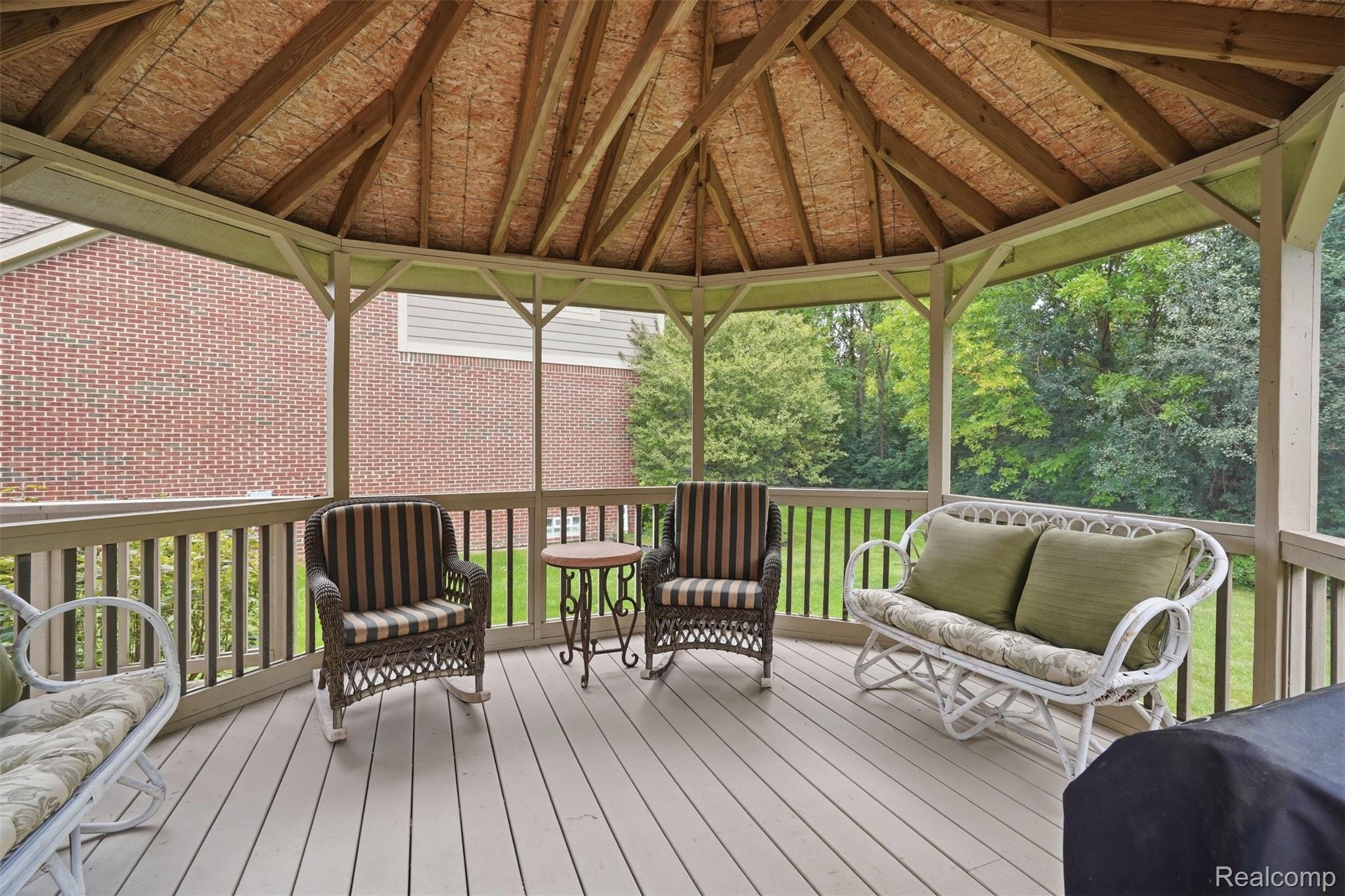 Covered deck with timber roof, wicker seating, and views of the lawn and trees.