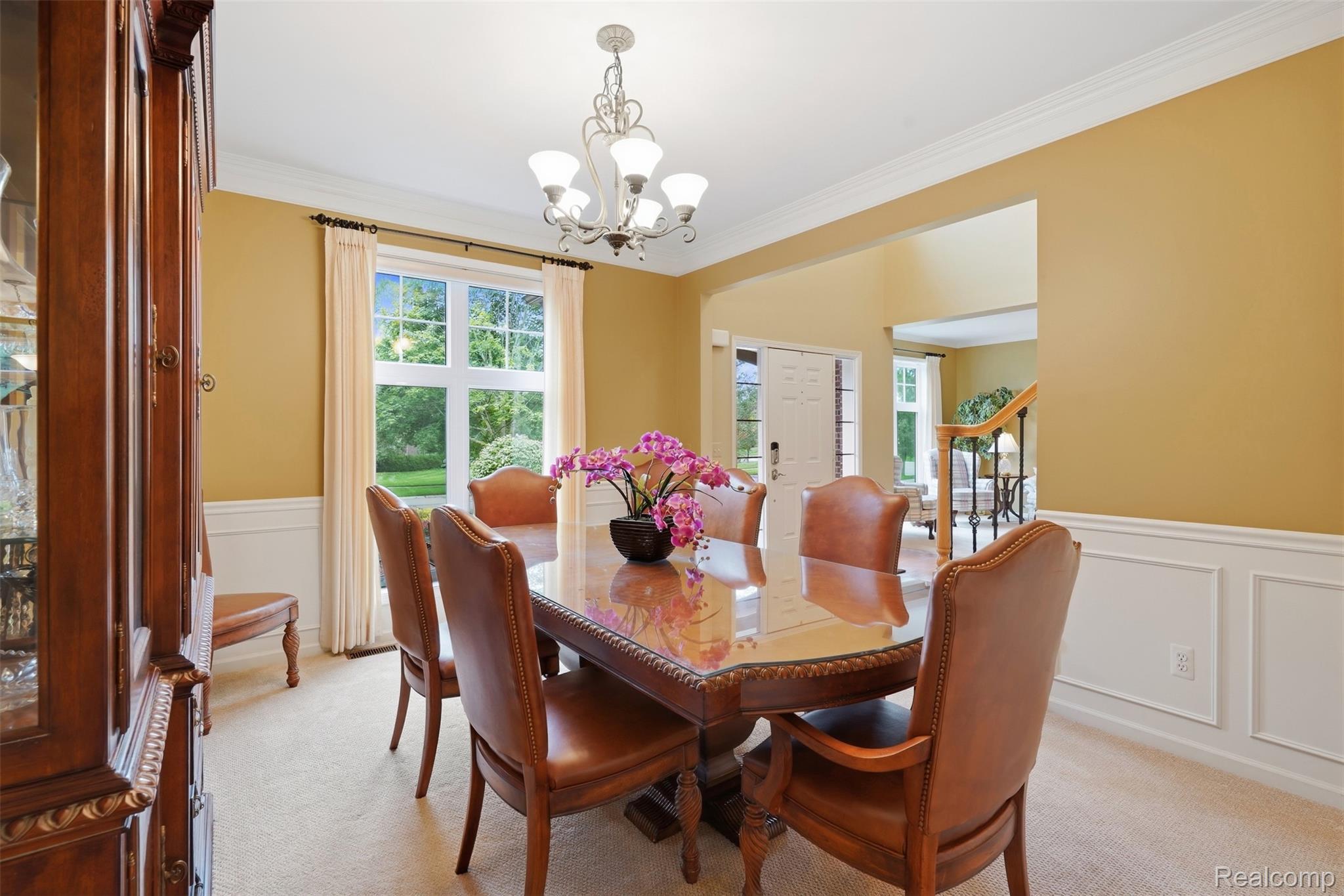 Dining room with a polished wood table, leather chairs, purple orchids, and tall curtained windows.