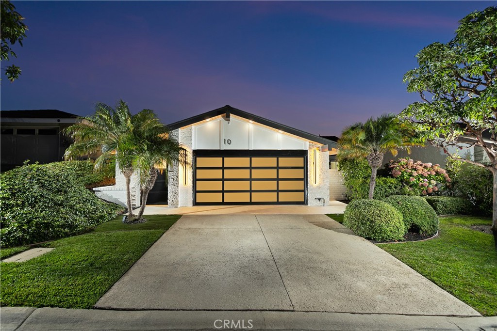 Modern home's illuminated front exterior with a gold-paneled garage door and landscaped driveway at dusk.