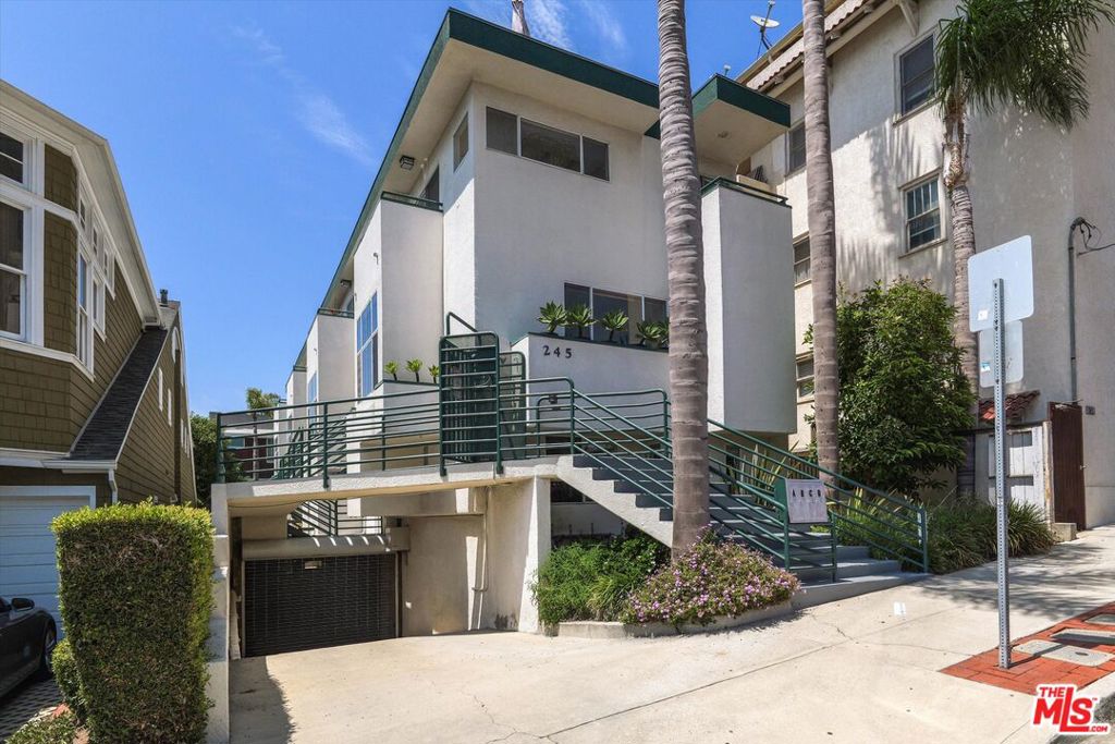 Multi-story residential building at 245 with elevated entry stairs, green railings, and palm trees.