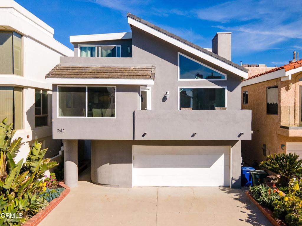 Modern gray two-story home with an asymmetrical roof, large windows, balcony, and attached garage.