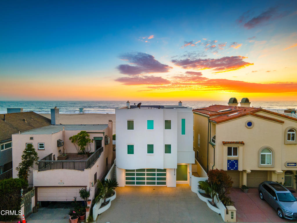 Coastal homes facing the ocean at sunset, with a white multi-story home centered in view.