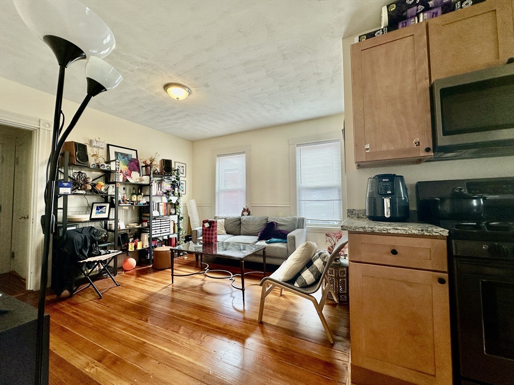 Living area with hardwood floors, a gray sofa, open shelving, and a compact kitchen.