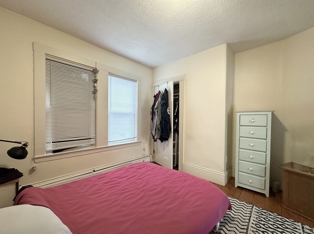 Bedroom with a pink bedspread, two windows, an open closet, and hardwood floors.