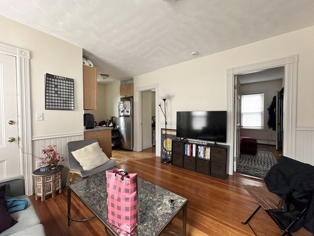 Living room with hardwood floors, a television and media console, and an open view into the kitchen.