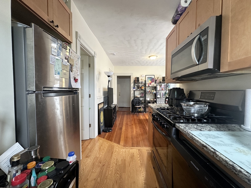 Galley kitchen with stainless-steel appliances, wood cabinets, and hardwood floors.