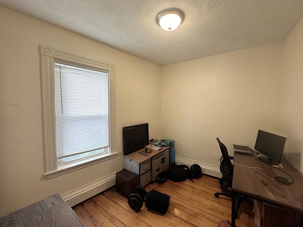 Home office with a desk and monitors beside a window, featuring hardwood floors.