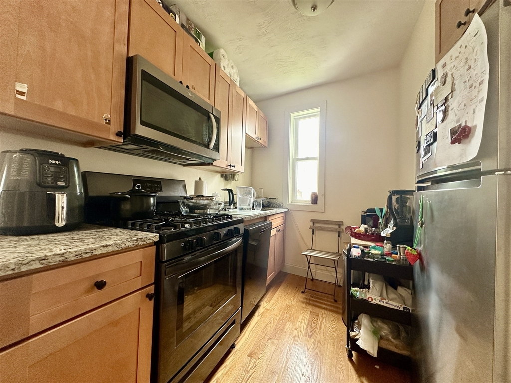 Narrow kitchen with wood cabinets, granite counters, stainless-steel appliances, and a tall window.