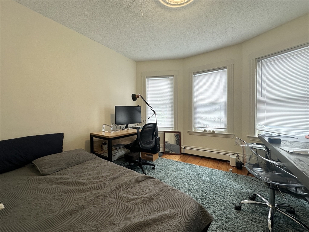 Bedroom with a bed, desk workstation, three windows with blinds, and a teal rug.