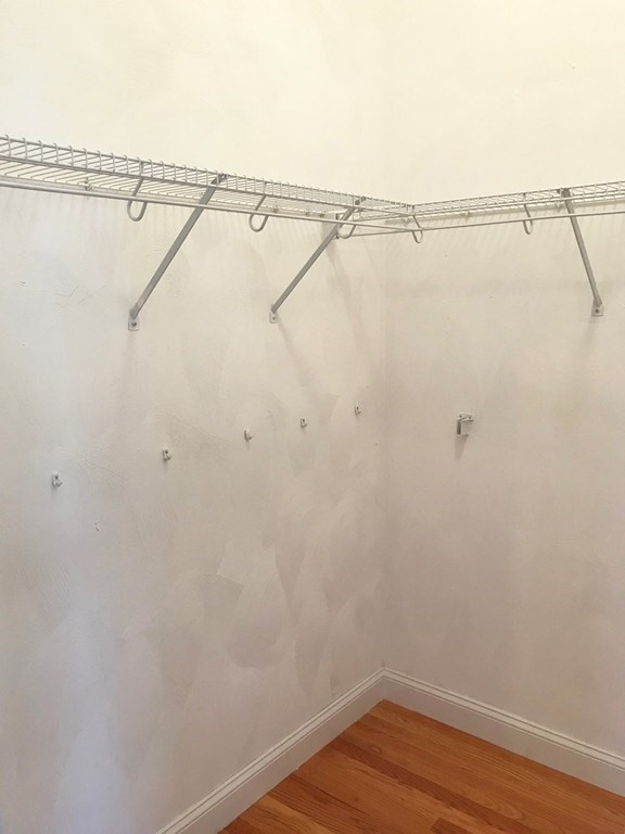 Empty closet with a wire shelf, hanging rod, wall hooks, and wood flooring.