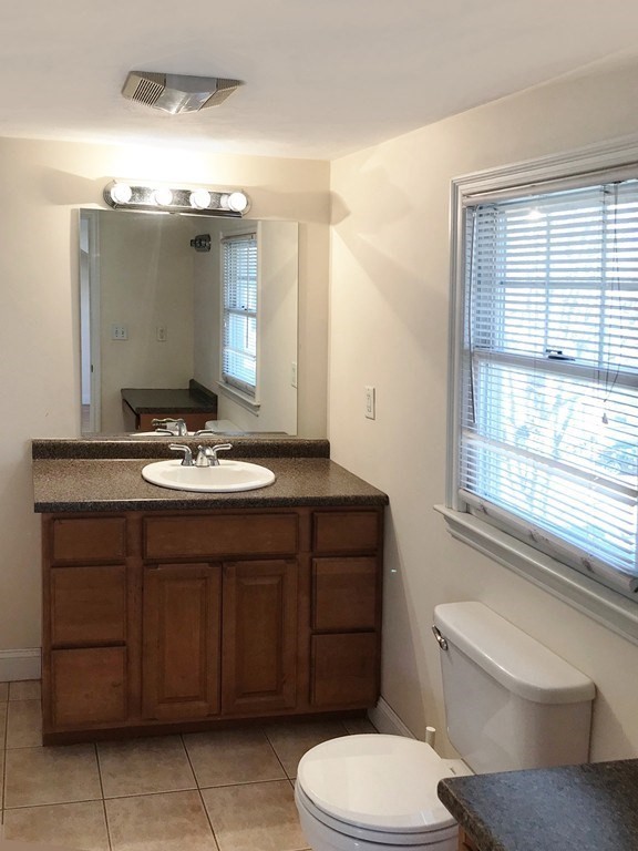 Bathroom with a wood vanity, large mirror, tiled floor, and window with blinds.