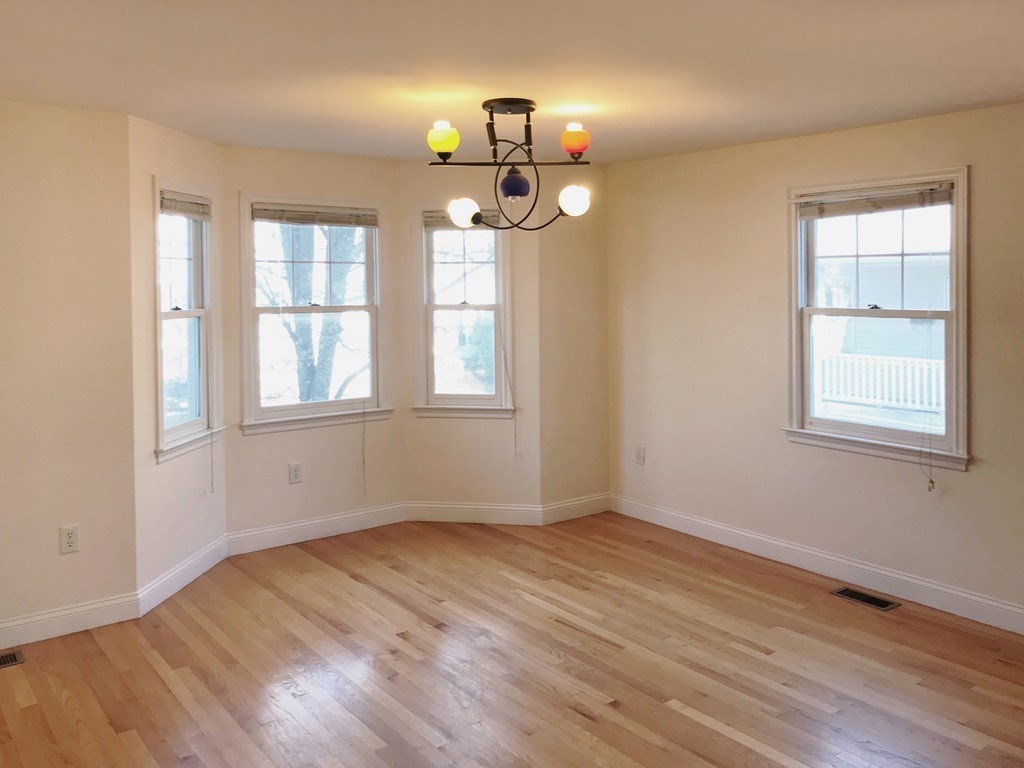 Empty dining room with hardwood floors, multiple windows, and a colorful chandelier.