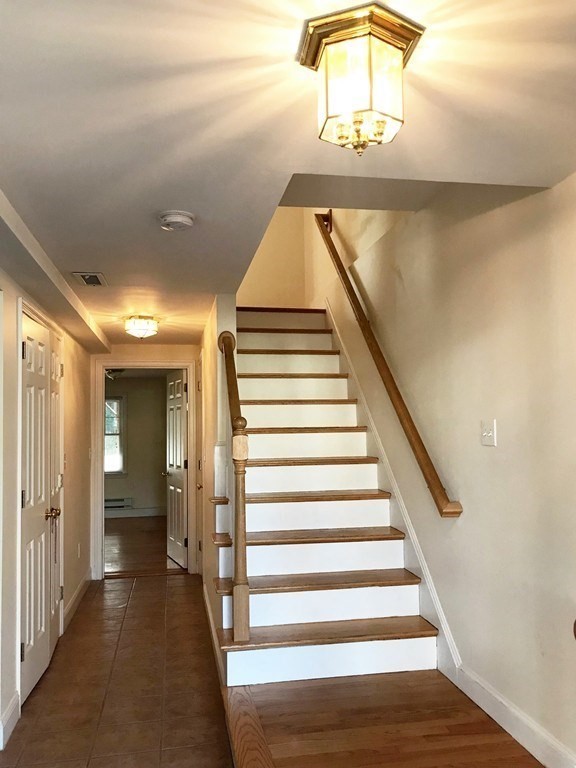 Hallway with a wood-trimmed staircase, tiled floor, and two ceiling lights.