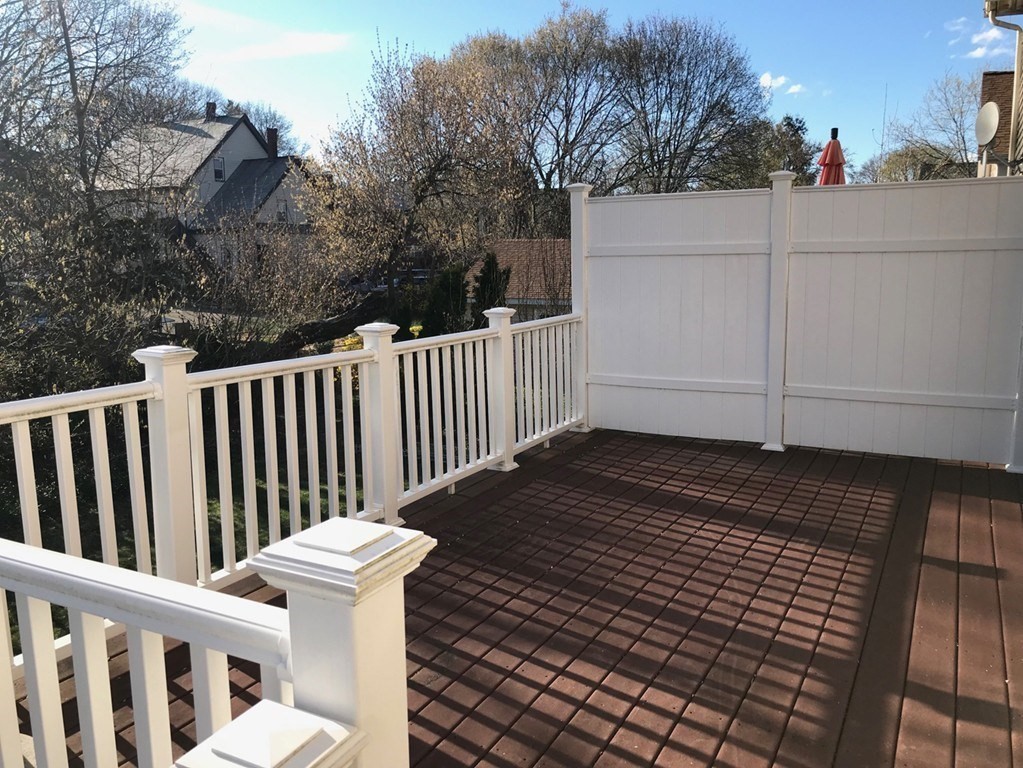 Elevated deck with dark brown decking, white railings, and a tall privacy fence.