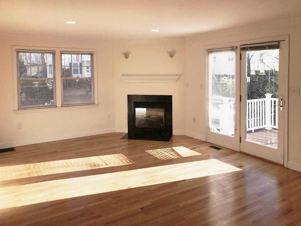 Vacant living room with hardwood floors, a black fireplace, and glass doors opening to a deck.