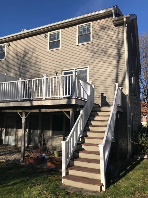 Rear of a beige two-story home with a raised white deck and long staircase.