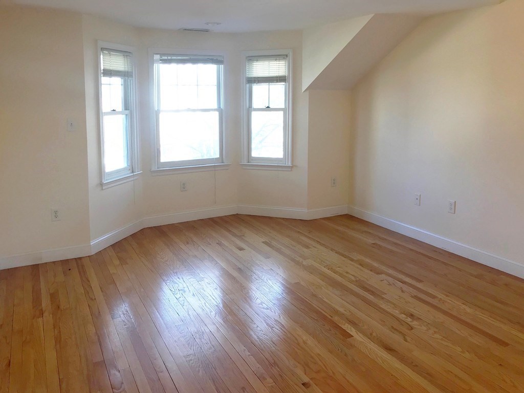 Unfurnished room with polished hardwood floors and three bay windows.