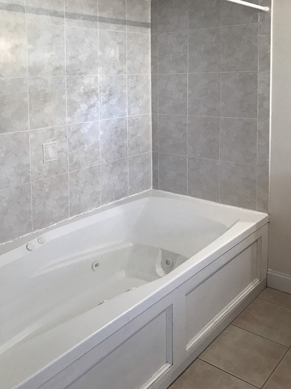 Bathroom with a white jetted bathtub and gray tiled walls.