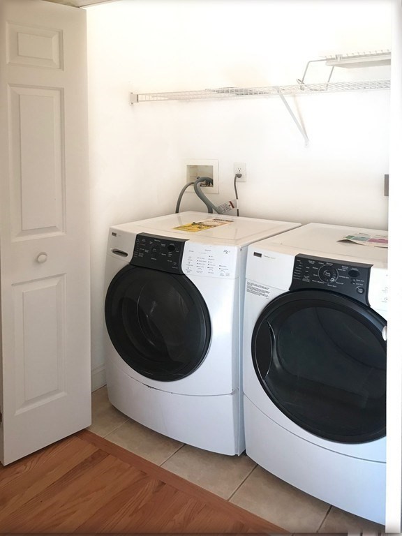 Laundry room with front-loading washer and dryer beneath a wall-mounted shelf.