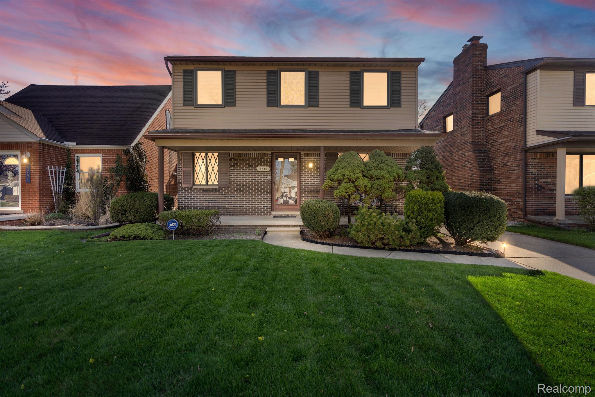 Two-story brick-and-siding house with a covered porch and landscaped front yard at dusk.