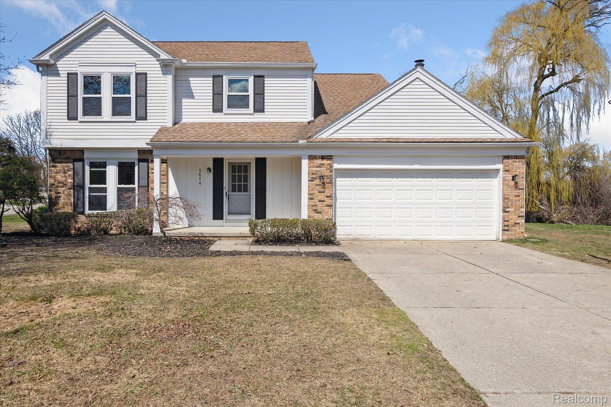 Two-story white-sided house with brick accents, dark shutters, and an attached two-car garage.