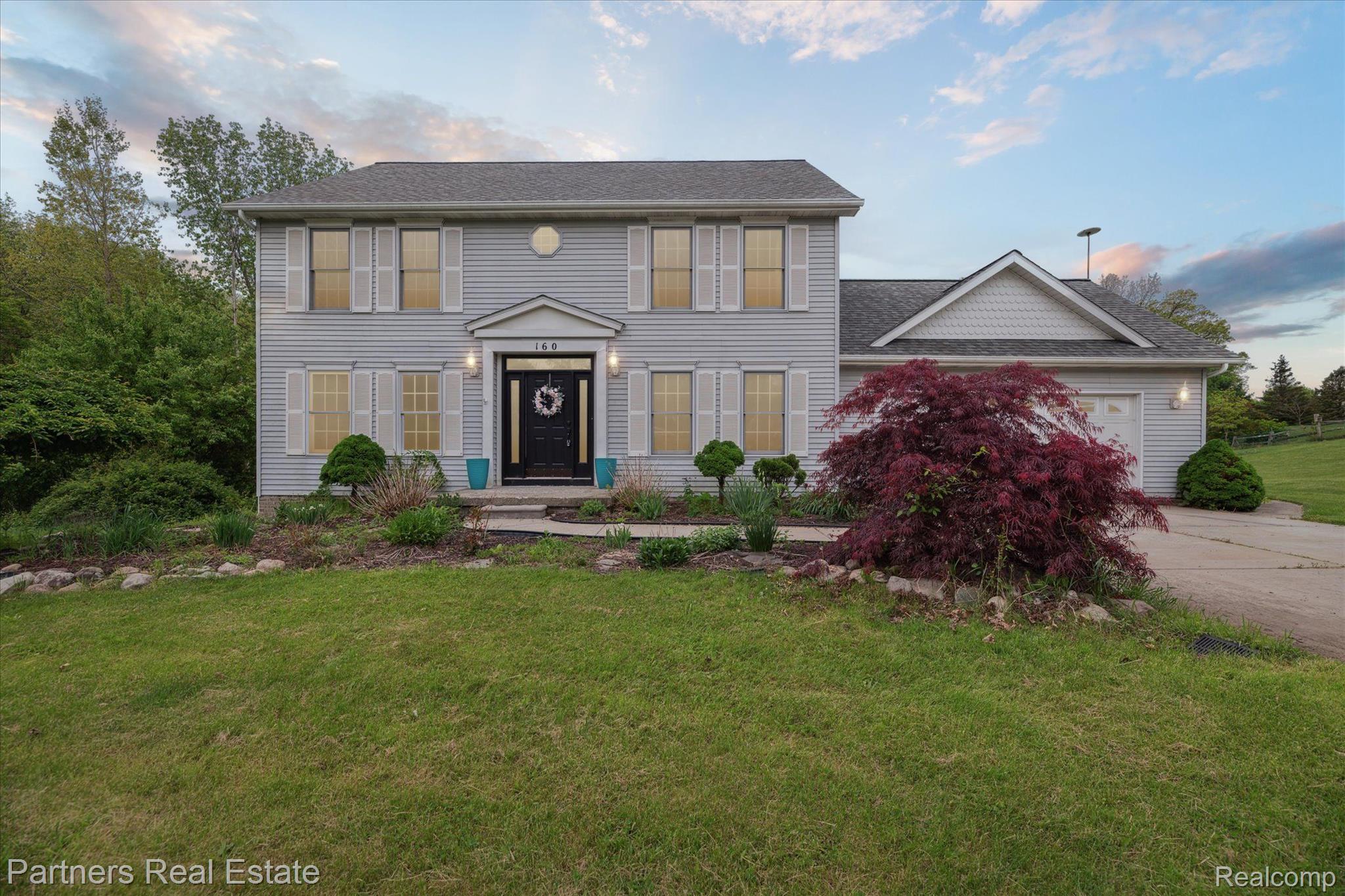 Two-story gray house with an attached garage and a landscaped front yard with a burgundy ornamental tree.