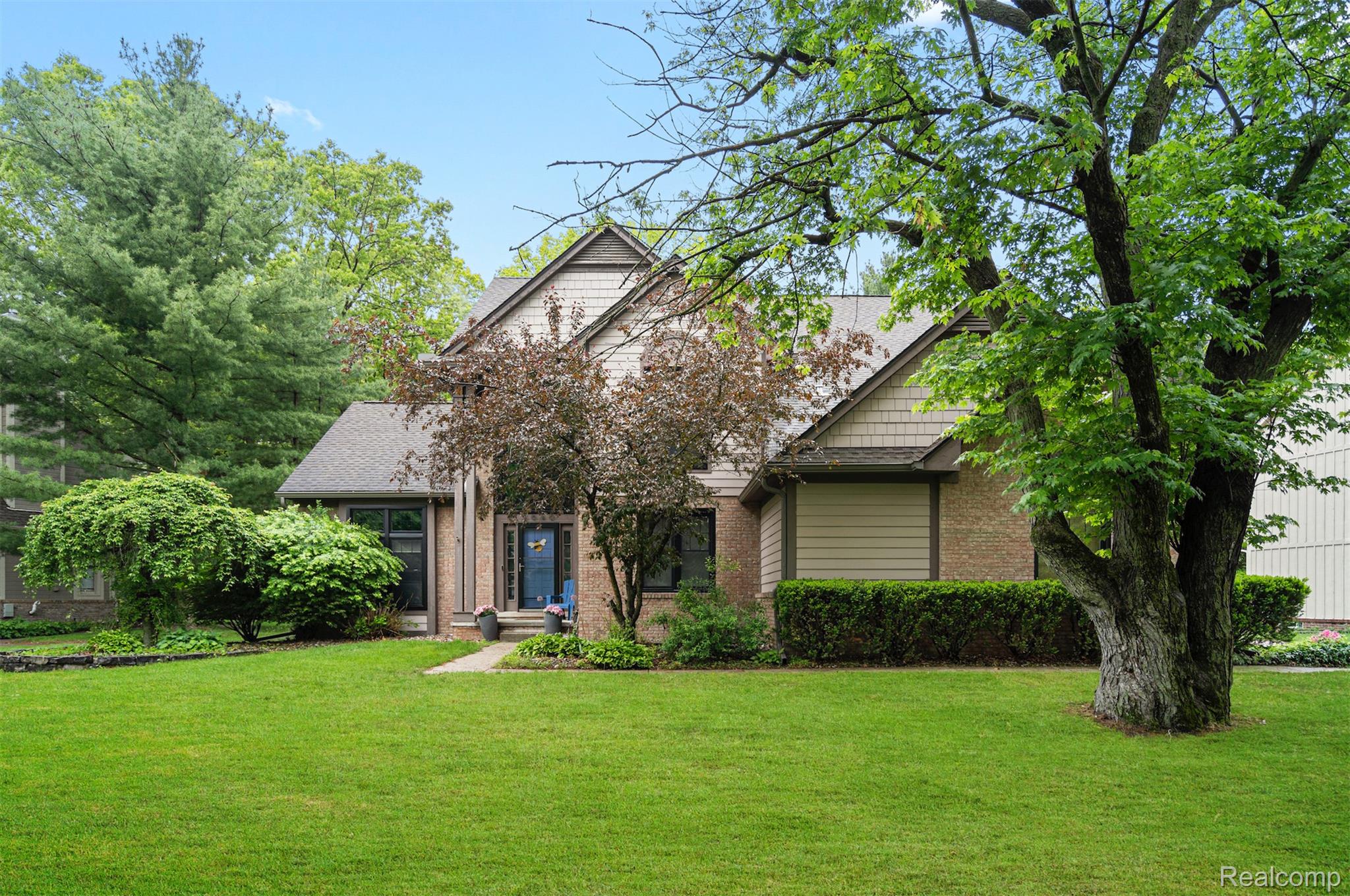 House with a blue front door, brick and siding exterior, and mature trees across the lawn.