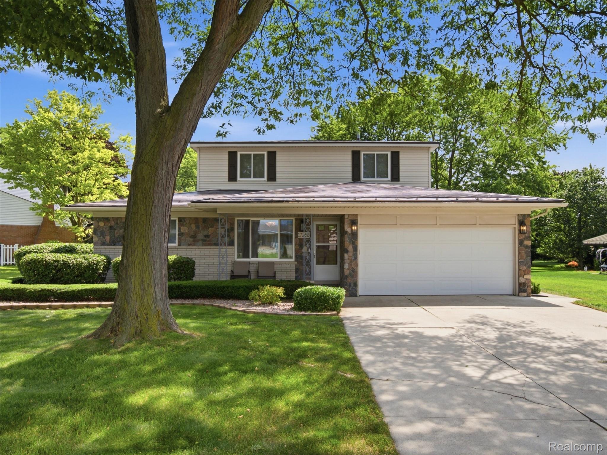 Two-story house with stone accents and white garage, partly shaded by a large front-yard tree.