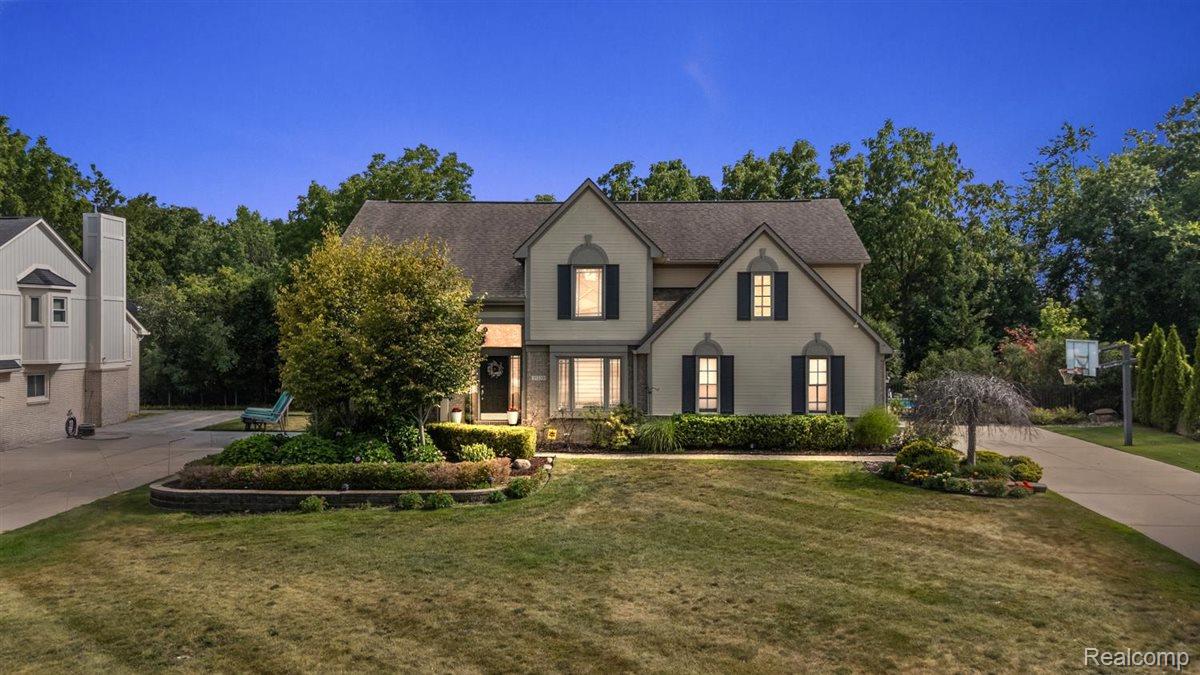 Two-story gray house with dark shutters, landscaped gardens, and a broad front lawn.