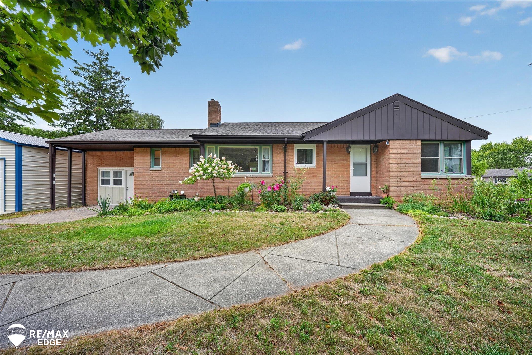 Brick ranch house with a dark gabled roof, flower beds, and a curved walkway.