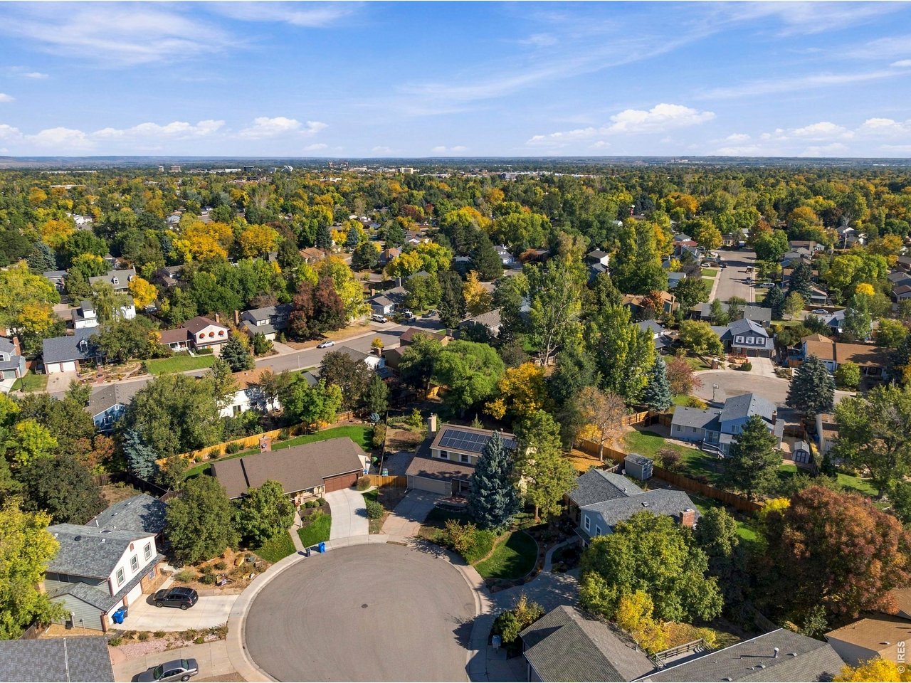 Aerial view of a tree-lined neighborhood and cul-de-sac beneath a wide blue sky.