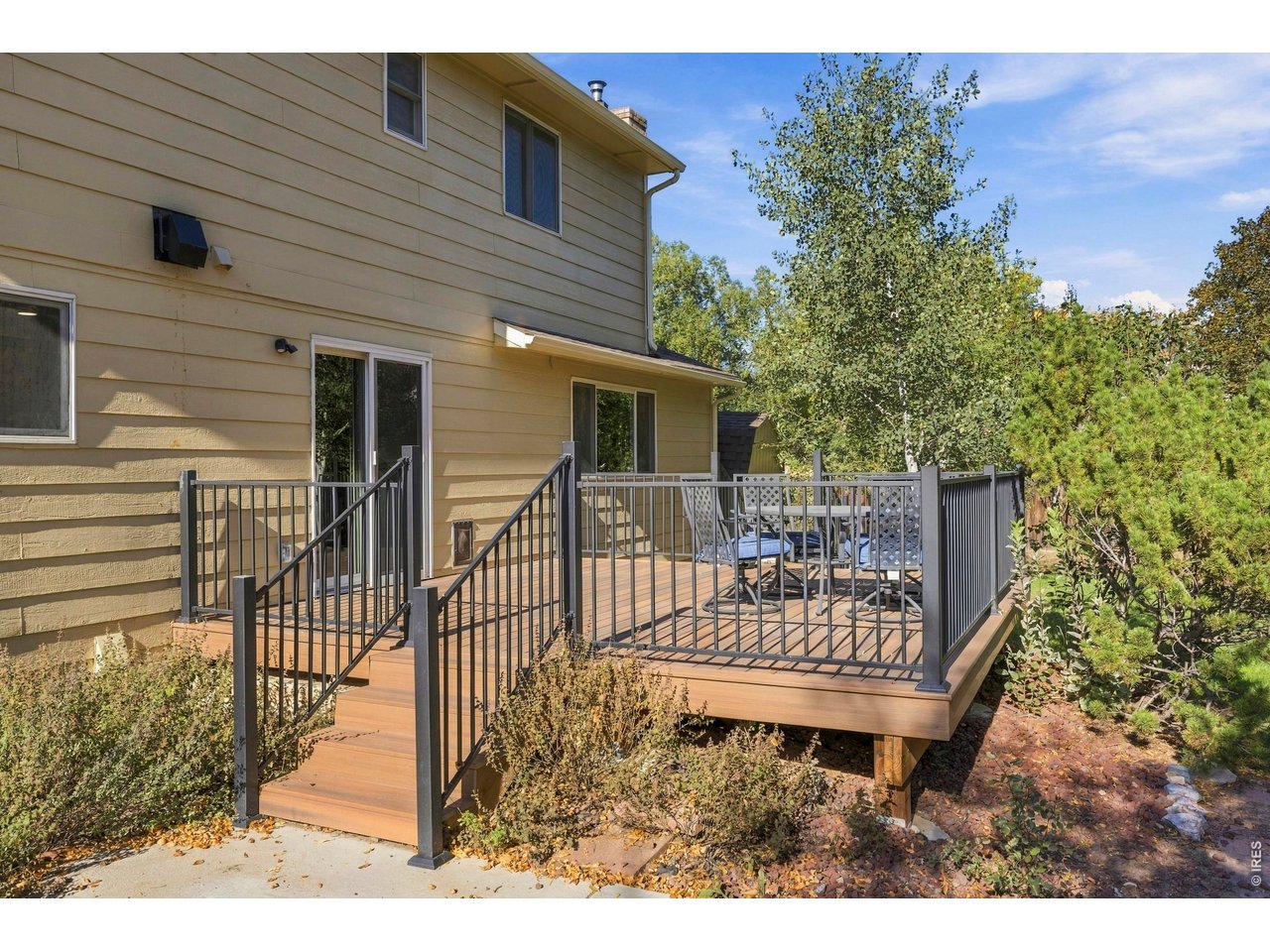 Raised wooden deck with black railings and patio furniture beside a tan-sided house.