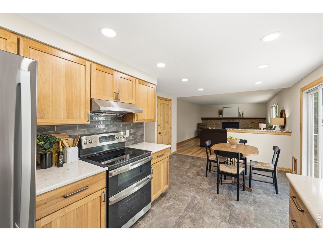 Kitchen with honey-colored cabinets and stainless steel appliances, opening to a dining area and brick fireplace.