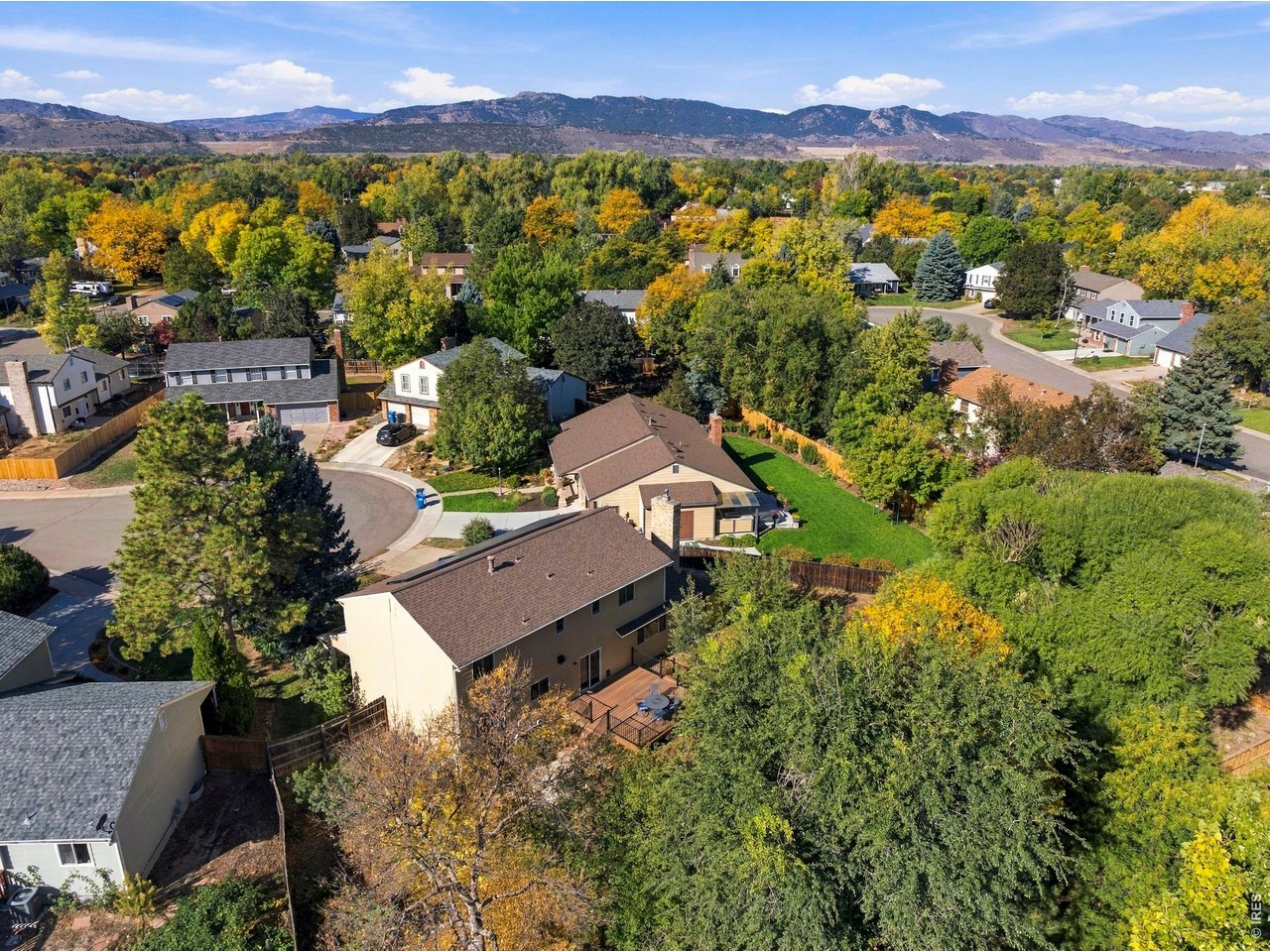 Aerial view of a home among autumn trees, with a neighborhood and mountain range beyond.