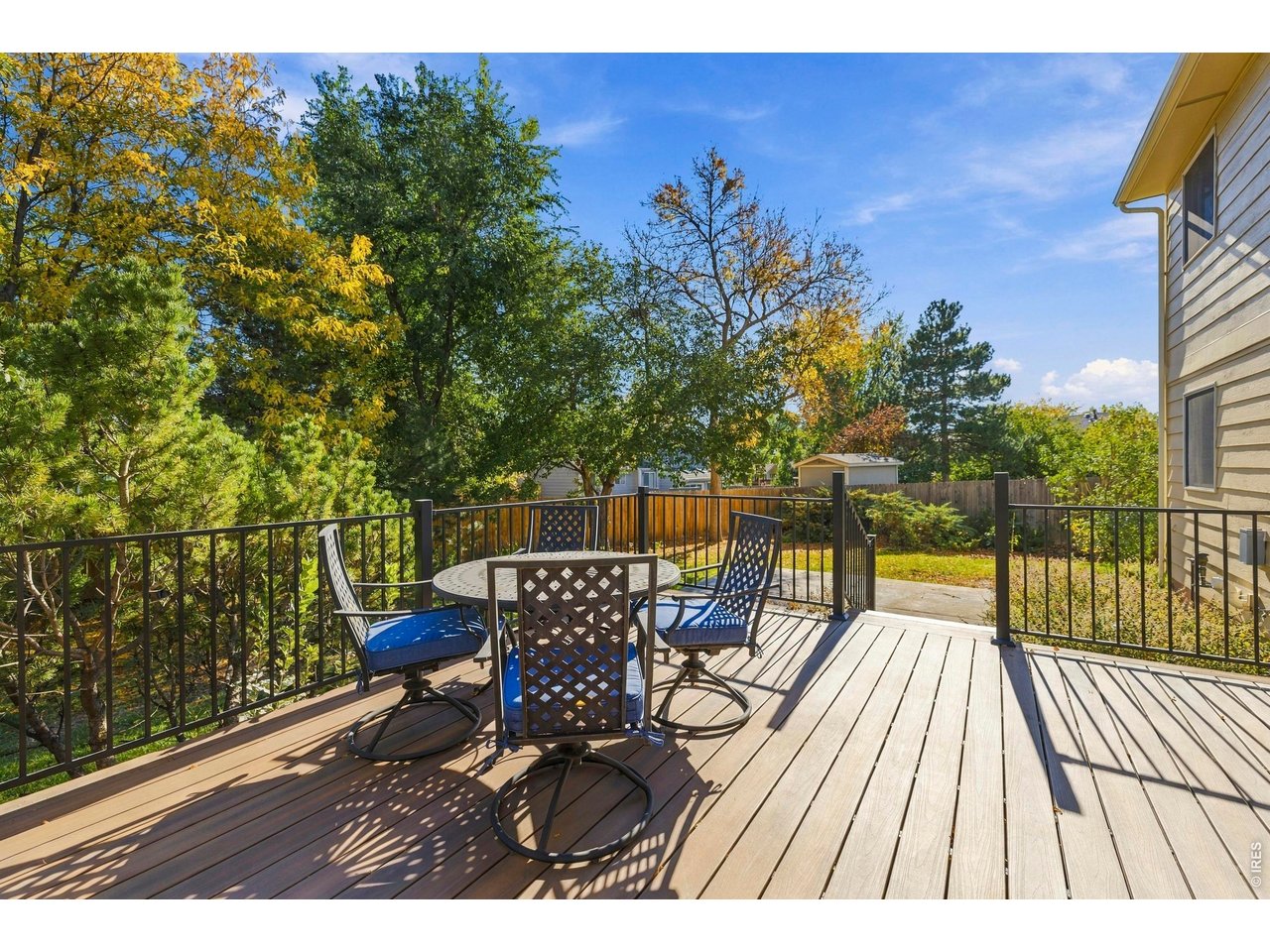 Raised wooden deck with a patio dining set, black railings, and autumn trees in the backyard.