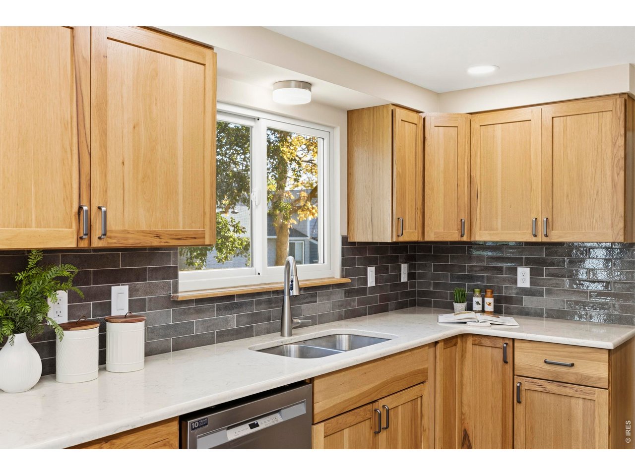Kitchen with natural wood cabinets, white countertops, dark tile backsplash, and a window overlooking autumn foliage.