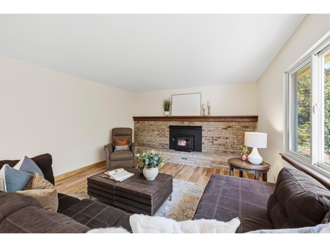 Living room with a brick fireplace, dark sofas, and a large window.