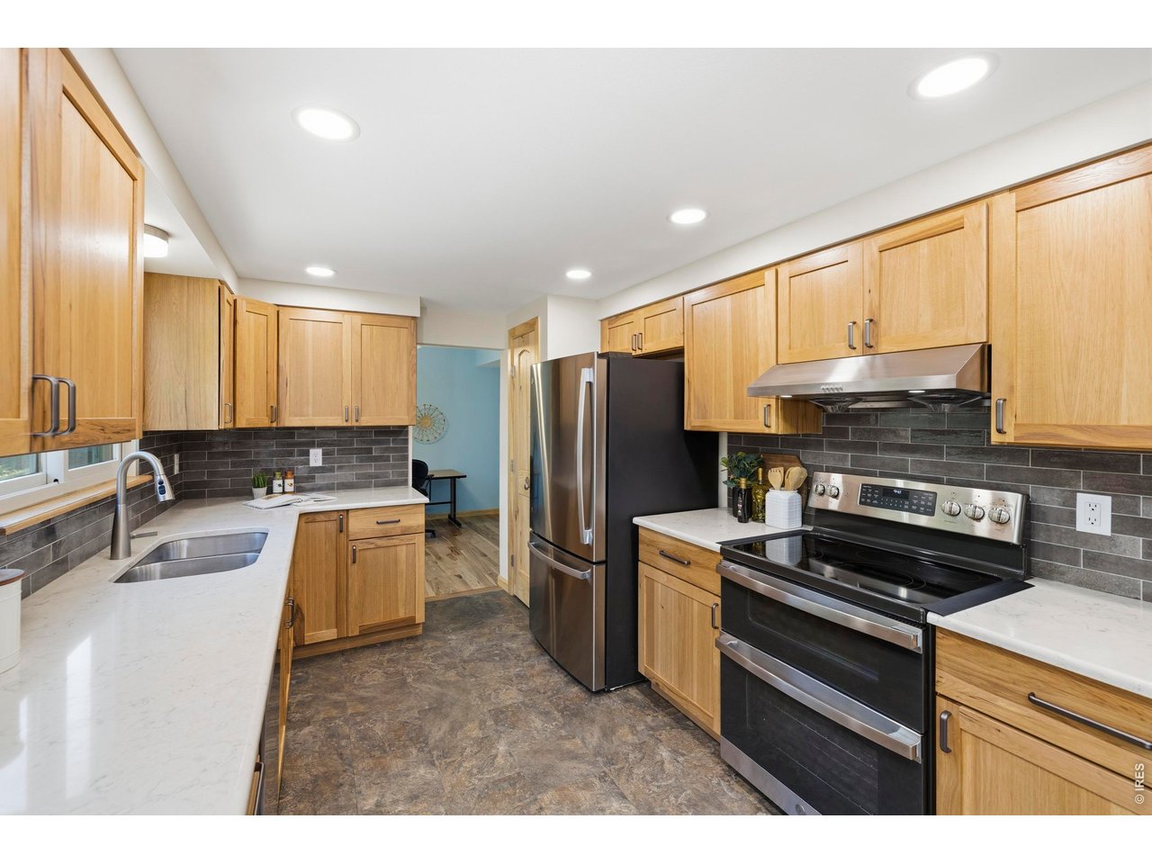 Kitchen with light wood cabinetry, white counters, dark tile backsplash, and stainless steel appliances.