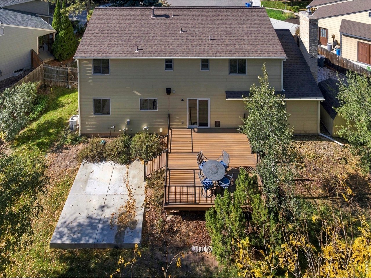 Rear of a two-story home with a raised deck, patio table, and concrete patio.
